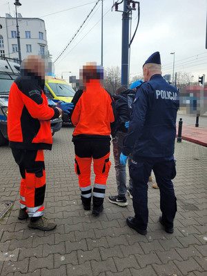 Zdjęcie przedstawia dwóch ratowników medycznych i policjanta, którzy prowadzą przed sobą mężczyznę.