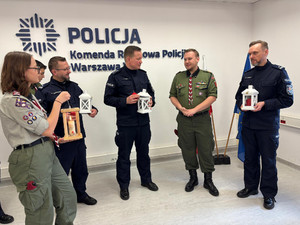 Na zdjęciu widać umundurowanych policjantów i harcerzy, którzy trzymają w dłoniach latarenki.