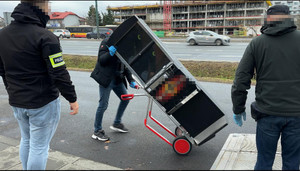 Zdjęcie przedstawia trzy osoby transportujące automat do gier.