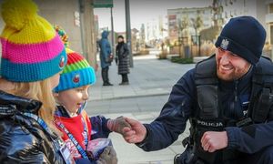 Zdjęcie przedstawia umundurowanego policjanta, który podaje rękę małej dziewczynce.