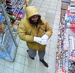 Zdjęcie przedstawia mężczyznę ubranego w musztardową kurtkę, szare spodnie, ciemne buty i białe rękawiczki.