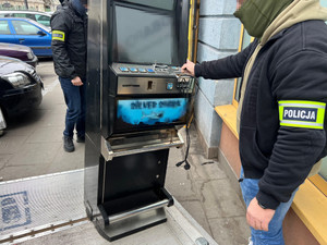 Zdjęcie przedstawia osobę z odblaskową opaską na przedramieniu, która zabezpiecza automat.