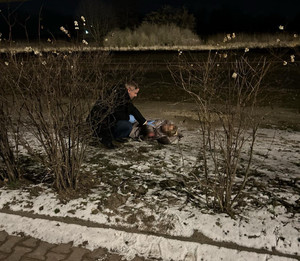 Zdjęcie przedstawia mężczyznę pochylającego się nad leżącą na ziemi kobietą.