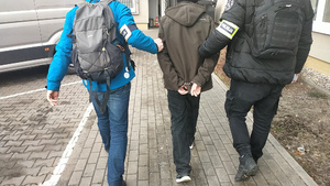 policjanci prowadzą pomiędzy sobą zatrzymanego mężczyznę.