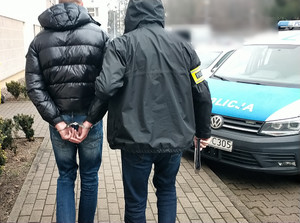policjant prowadzi po dziedzińcu zatrzymanego mężczyznę.