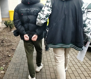 policjant prowadzi po dziedzińcu zatrzymanego mężczyznę.