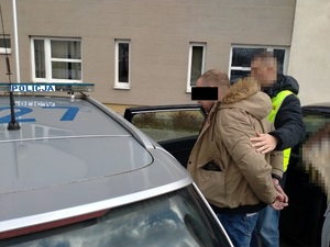 Zdjęcie przedstawia policjanta prowadzącego do radiowozu zatrzymanego mężczyznę.