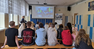 Zdjęcie przedstawia policjantkę stojącą przed uczniami siedzącymi w ławkach.
