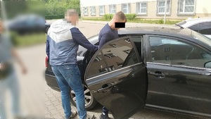 Zdjęcie przedstawia policjanta, który umieszcza zatrzymanego mężczyznę na tylnym siedzeniu samochodu.