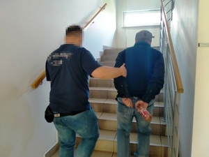Zdjęcie przedstawia policjanta prowadzącego po schodach zatrzymanego mężczyznę.