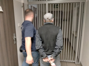 Zdjęcie przedstawia policjanta wyprowadzającego zatrzymanego mężczyznę z pomieszczenia dla osób zatrzymanych.