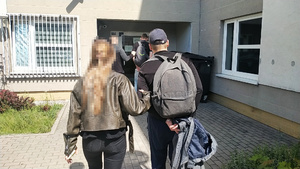 Zdjęcie przedstawia dwoje policjantów, którzy prowadzą po swojej prawej stronie dwóch zatrzymanych mężczyzn.