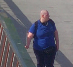 Mężczyzna na zdjęciu ma 25-35 lat. Mężczyzna jest łysy, bez widocznego zarostu na twarzy. Ubrany jest w niebieską koszulkę z krótkim rękawem i ciemne spodnie.