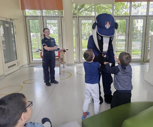 Zdjęcie przedstawia policjantkę i misia Borsuka stojących przed dziećmi. Borsuk podaje łapy dwóch chłopcom.