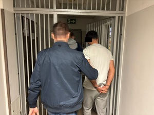 Zdjęcie przedstawia policjantów w ubraniach cywilnych, którzy wyprowadzają z pomieszczenia zatrzymanego mężczyznę.