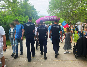 Zdjęcie przedstawia trzech policjantów idących wśród ludzi.