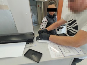 Zdjęcie przedstawia policjanta, który wykonuje daktyloskopię u kobiety.