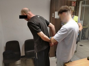 Zdjęcie przedstawia policjanta zakładającego zatrzymanemu kajdanki na ręce trzymane z tyłu.