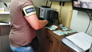 Zdjęcie przedstawia fragment sylwetki policjanta stojącego obok szafki na której leżą banknoty.