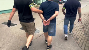 Zdjęcie przedstawia policjantów prowadzących zatrzymanego mężczyznę.