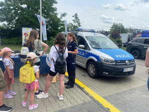 Policjantka stoi pomiędzy radiowozem a grupą dzieci.