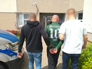 Zdjęcia przedstawia policjantów prowadzących chodnikiem pomiędzy sobą zatrzymanego ubranego w zieloną bluzę.