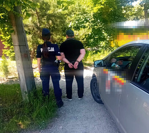 Zdjęcie przedstawia umundurowaną policjantkę prowadzącą po swojej prawej stronie zatrzymanego mężczyznę.