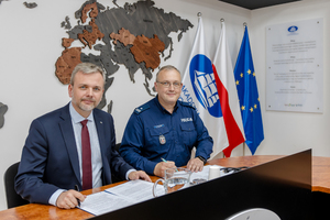 Zdjęcie przedstawia policjanta i mężczyznę w garniturze siedzących przy jednym stole.