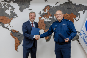 Zdjęcie przedstawia policjanta i mężczyznę w garniturze podających sobie dłonie.