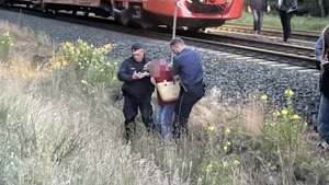 Policjanci pomagają kobiecie przejść przez nasyp kolejowy.