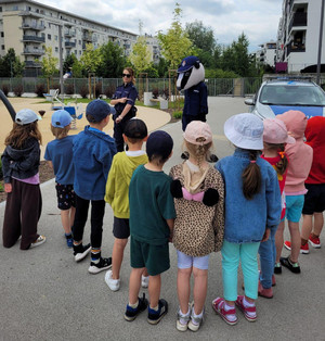 Zdjęcie przedstawia policjantkę, misia Borsuka i dzieci stojące na szkolnym boisku obok radiowozu.