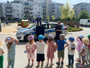 Zdjęcie przedstawia policjantkę, misia Borsuka i dzieci stojące na szkolnym boisku obok radiowozu.