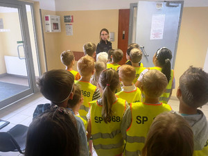 Zdjęcie przedstawia policjantkę stojącą z dziećmi przed uchylonymi drzwiami do pomieszczenia.