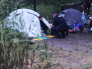 Zdjęcie przedstawia policjanta rozmawiającego z osobą wychylającą się z namiotu.