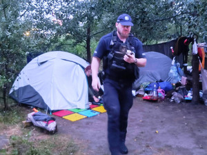 Zdjęcie przedstawia policjanta idącego przez dzikie obozowisko.