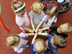 Zdjęcie przedstawia dzieci stojące w kółku, które wyciągają przed siebie ręce z odblaskami.