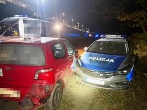 Zdjęcie przedstawia dwa uszkodzone pojazdy stojące obok siebie - czerwoną toyotę i oznakowany radiowóz.