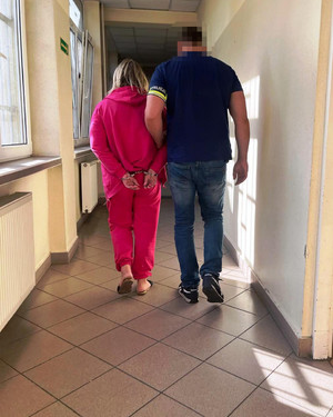 Policjant prowadzi po swojej lewej stronie zatrzymaną kobietę.