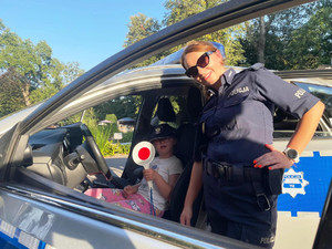 Zdjęcie przedstawia policjantkę stojącą przy radiowozie, w którym siedzi dziecko.