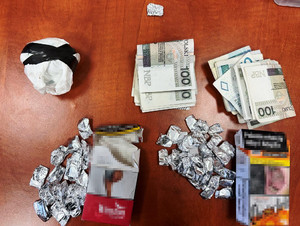 Zdjęcie przedstawia srebrne zawiniątka, gotówkę, paczki papierosów leżące na brązowym blacie stołu.