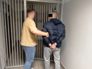 Zdjęcie przedstawia policjanta wyprowadzającego z pomieszczenia dla osób zatrzymanych mężczyznę.