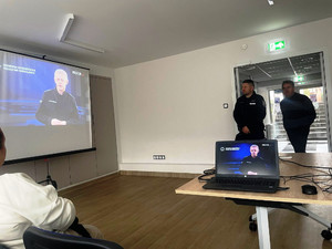 Zdjęcie przedstawia policjanta i mężczyznę stojących w sali.