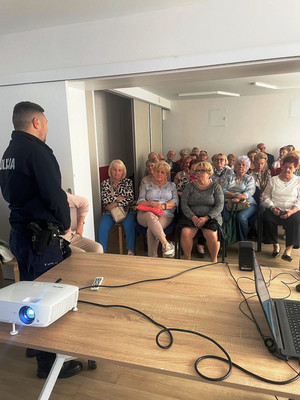 Zdjęcie przedstawia policjanta stojącego przed grupą seniorów.