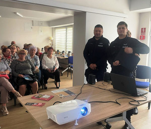 Zdjęcie przedstawia policjantów i siedzących za nimi na krzesłach seniorów.