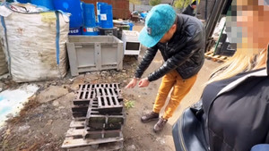 Zdjęcie przedstawia mężczyznę pochylającego się nad włazami do studzienek kanalizacyjnych.