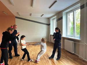 Zdjęcie przedstawia dzieci trzymające kajdanki i dorosłych, w tym policjantów stojących obok nich.