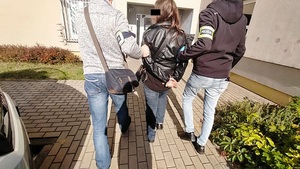 Policjanci prowadzą zatrzymaną kobietę.