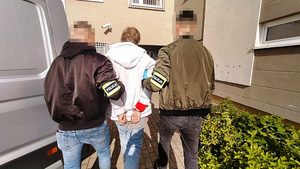 Policjanci prowadzą przez parking zatrzymanego mężczyznę.