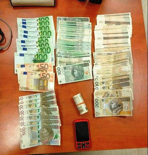 Zdjęcie przedstawia gotówkę w EURO I polskiej walucie rozłożoną na brązowym blacie stołu. Tuż pod nią leży ciemny telefon komórkowy.