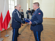 Zdjęcie przedstawia dwóch umundurowanych galowo policjantów, którzy podają sobie ręce.